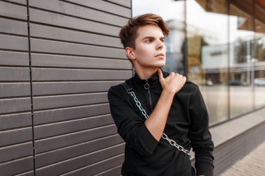 Şık yakışıklı genç bir siyah şık Kazak bir çanta içinde bir saç modeli ile şehirde yürür