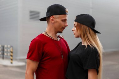 Güzel genç şık hipster çift giyimleri beyzbol kapaklar ile sokakta duruyor