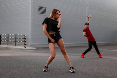 Siyah şık elbiseleri genç güzel dansçı kız dışarıda dans ediyor. Arka planda erkek dansçı