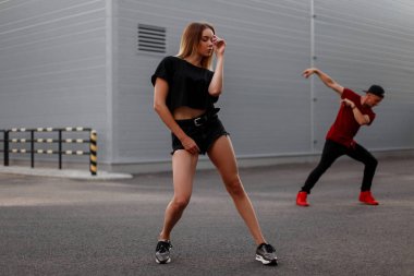 Dışarıda dans siyah moda giysileri ile şık güzel genç hip hop kadın dansçı. Dansçı adam arka planda