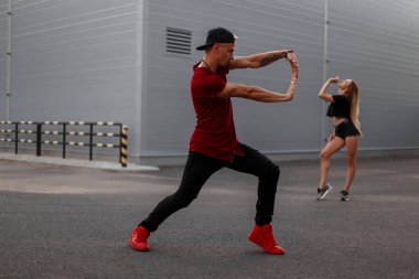 Yakışıklı genç dansçı bir beyzbol şapkası kırmızı kolsuz bluz, siyah kot ve kırmızı ayakkabılar ile sokakta dans ediyor. Arka plan üzerinde kadın dansçı