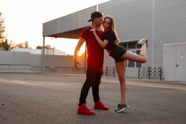 Beyzbol kapaklar moda giysiler dansları ve sokak gün batımında hugs şık genç çift