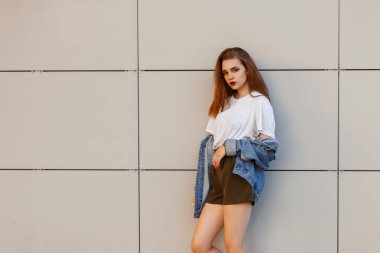 Vintage kot şort modern bir duvarının yakınında olan gri bir tişört giysileriyle moda güzel genç şık kadın modeli