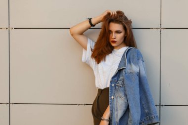 şık denim kot pantolon giysili genç kızı bir duvara yakın duruyor