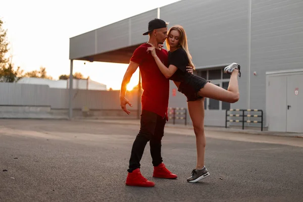 Beyzbol kapaklar moda giysiler dansları ve sokak gün batımında hugs şık genç çift
