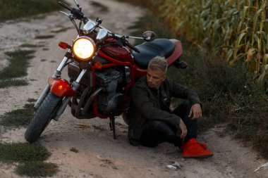 bir şık askeri haki ceketli adamı yakışıklı genç model bir motosiklet akşam ışık bir alanda ile oturuyor. Kavram seyahat