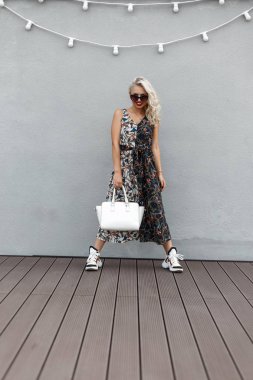 Beyaz bir şık çanta trendy elbise ve spor ayakkabı gri duvara yakın poz ile güneş gözlüklü zarif güzel genç model kız