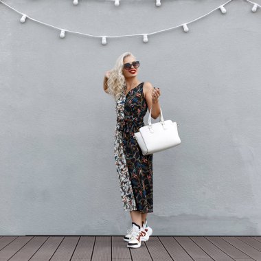 Bununla birlikte güneş gözlüklü bir gri duvarının yakınında şık elbiseli şık güzel ve genç birbayan