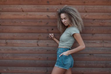 Moda denim giysileri ahşap duvarının yakınında şık güzel genç kıvırcık hipster moda kadın