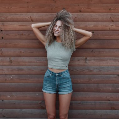 Komik mutlu hipster kadın moda kot elbise bir ahşap duvar yakınındaki bir gülümseme kıvırcık saçlı