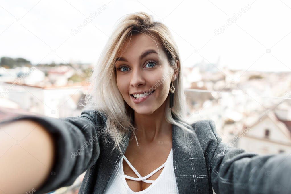 Surprised funny beautiful young woman with a smile in a vintage suit doing selfie on camera in the city. Girl blogger travels in the city and shoots