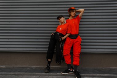 Genç güzel şık çift modelleri moda kapaklar ve trendy Turuncu elbise gri duvara yakın duruyorsun