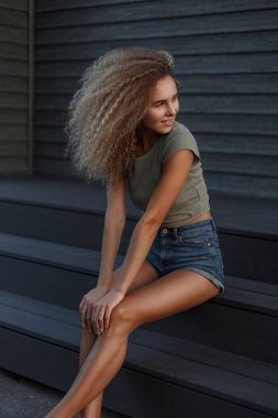 Mutlu güzel komik kıvırcık kadın seksi kot denim şort merdivenlerde oturan bir gülümseme