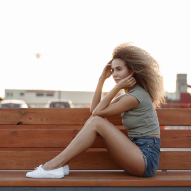 Bir bankta oturan ince seksi bacaklar ile kot şortlu kıvırcık saçlı güzel şık kadın