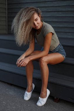 Güzel seksi moda kıvırcık model kadın kot şort merdivenlerde oturan güzel bacaklar ile