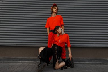 Kapaklar gri metal duvara yakın poz spor ayakkabıları ile turuncu giyimleri şık güzel genç çiftle