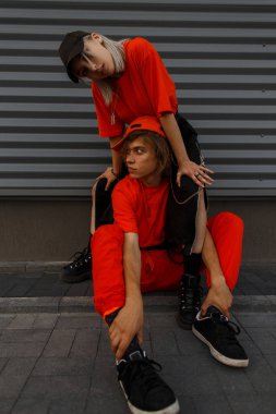 Kapaklar gri duvarın yanında turuncu şık giysileri ile şık genç çift