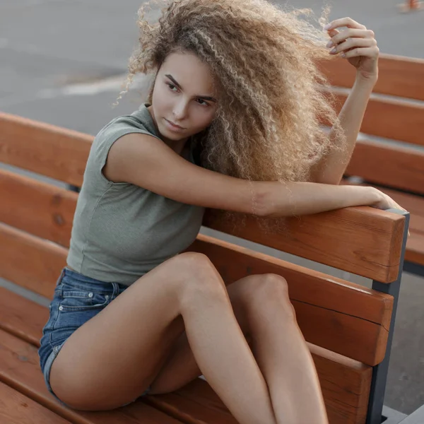 ベンチに座っているスリムなセクシーな脚でトレンディなジーンズ服美しい若いスタイリッシュなヒップスター中女性 — ストック写真