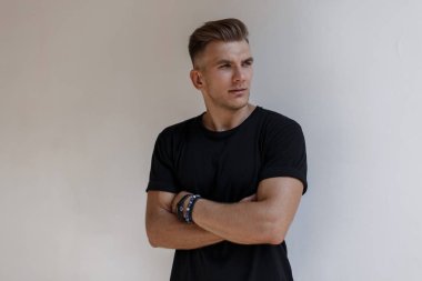 Siyah moda saç modeliyle şık yakışıklı genç portresi t-shirt duvara yakın duruyor.