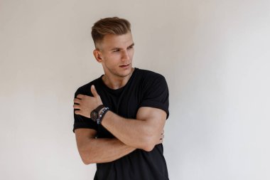 Moda yakışıklı genç bir siyah saç modeli ile t-shirt bir saati olan beyaz bir duvar sokak yakınındaki poz veriyor