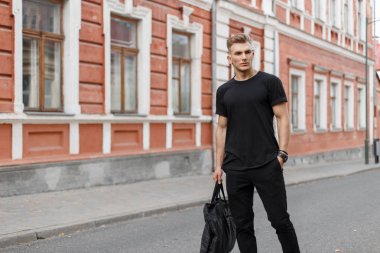 Siyah bir çanta ile siyah şık mockup giysili şık yakışıklı genç adam şehirde yürür