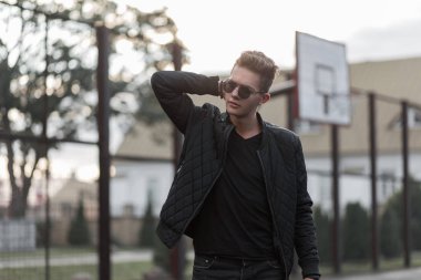 Şık yakışıklı genç trendy güneş gözlüğü ve sokakta basketbol Stadyumu'nda moda siyah giysiler ile 