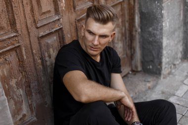 Siyah t-shirt şık yakışıklı genç adam ahşap vintage kapının yanında oturuyor.