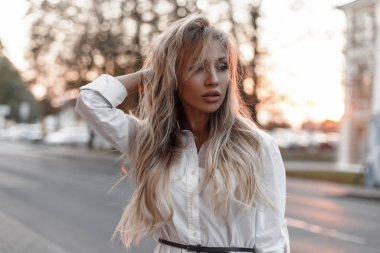 Güzel genç şık model kadın saç beyaz şık gömlek modeli ile sokakta günbatımında yürür.