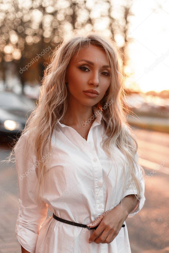 Stylish beautiful young model woman in a white shirt in the city at sunset