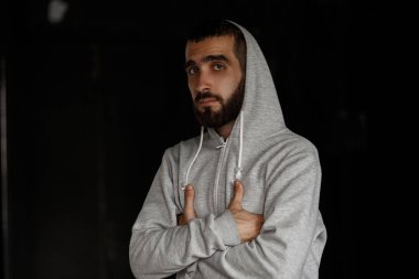 İçinde karanlık bir arka plan üzerinde gri kapşonlu sakallı şık yakışıklı genç adam