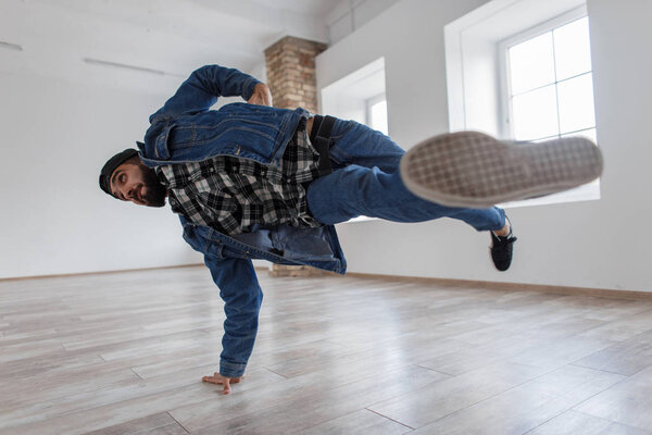 Young handsome stylish male dancer with a cap in denim fashionable clothes dancing breakdance in a dance studio