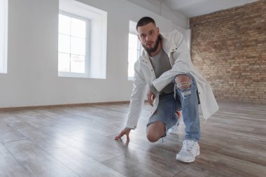 Moda çekici yakışıklı genç moda ceket ile poz ve kamera kapalı seyir beyaz spor ayakkabı ile yırtık kot pantolon