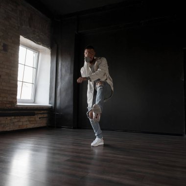Şık yakışıklı genç dansçı moda giysileri yırtık kot ile hip-hop karanlık bir arka plan bir dans stüdyosunda dans spor ayakkabı ile