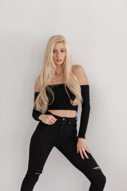 Beyaz duvar odadaki yakınındaki seksi genç sarışın siyah moda giysiler içinde poz veriyor