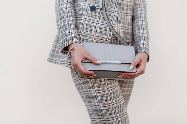 Красивая стильная молодая женщина с модной сумочкой и модным клетчатым костюмом позирует у стены
