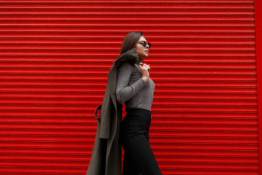 Yeşil bir ceket ve siyah gömlek kırmızı metal kapıları yanında vintage gri süveterli moda güneş gözlüğü ile şık genç ve güzel çekici kadın modeli