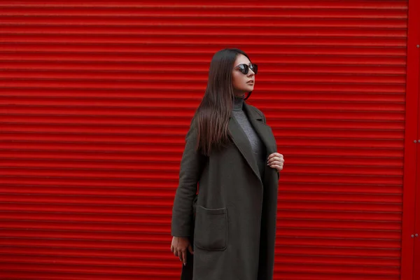 赤い金属ゲート付近緑ファッション コートでファッショナブルなサングラスをスタイリッシュな美しい若いビジネス女性 — ストック写真