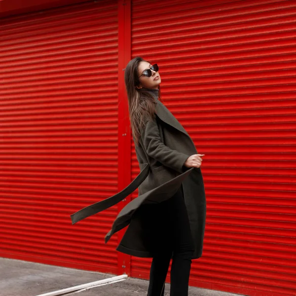 Genç güzel şık kadın moda yeşil ceket teşkil kırmızı metal arka plan yakınındaki şık güneş gözlüğü