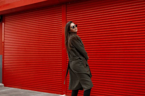 Moda yeşil paltolu kırmızı metal geçidin yakınlarında poz güneş gözlüklü genç moda güzel kadın modeli