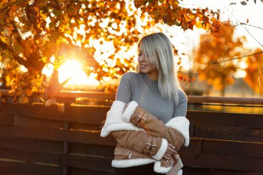 Poz ve altın ağaçlar güzel bir sonbahar günbatımı zevk fonunda gülümseyen bir gri şık vintage örme kazak gülümseme sevimli mutlu genç kadın. Çekici sarışın kız