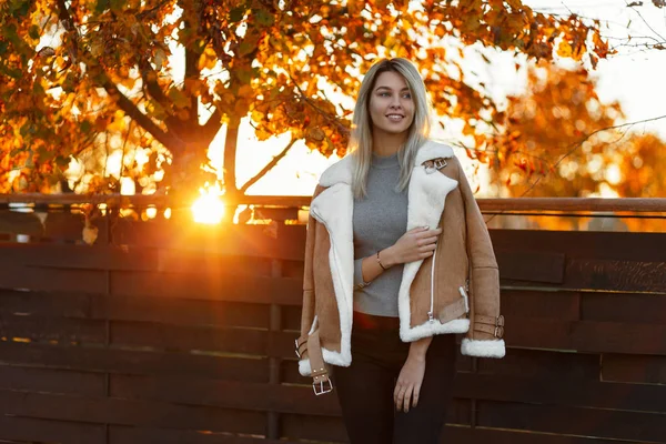 迷人的年轻快乐的女人在一个时尚的针织复古毛衣和秋天夹克摆在户外的公园在秋天的树木背景下日落 女孩微笑 — 图库照片