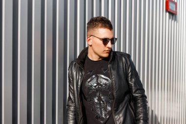 Şık şık yakışıklı genç hipster siyah deri ceket ve kazak gümüş metal duvar yakınındaki güneş gözlüklü