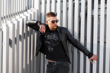 Gözlüklü metal borular duvarının yakınında bir deri moda ceket ile siyah giyimleri şık yakışıklı genç hipster adam 