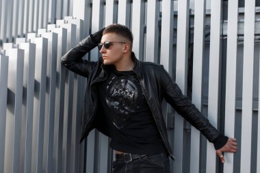 Şık şık genç hippi erkek güneş gözlüğü moda siyah ceket ve siyah kazak metal duvara yakın poz bir kafatası ile