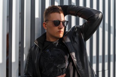 Güneş gözlüğü ve güneşli bir sonbahar günü Metalik arka plan üzerinde poz şık siyah ceket genç şık yakışıklı seksi hipster adam. Bir stil saç modeli ile çekici şık adam