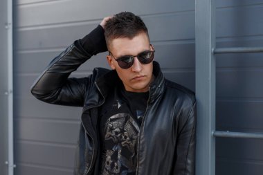 Saç siyah güneş gözlüğü ve siyah şık sonbahar giyim gri bir duvara yakın poz ile çekici genç şık hipster adam. Şık yakışıklı adam.
