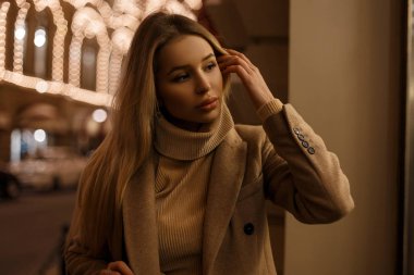 Sevimli genç kadın paltolu bir vintage moda şık sıcak sonbahar ve sıcak bej şık kazaklı gece ışıkları sokak poz. Şık sarışın kız