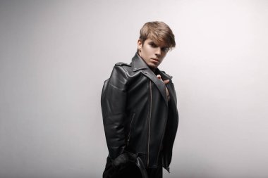 Yakışıklı genç çekici kırmızı şık golf ve şık siyah kot moda siyah deri ceketli bir saç modeli ve beyaz bir duvar yakınındaki bir odada poz duran adam. Tarzı modern adam