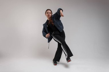 Şık spor giyim ve spor ayakkabı gösterir yeni dans hareketleri sınıf kamera için beyaz bir arka plan üzerinde yetenekli genç güzel kadın dansçı. Şık hippi kız dans