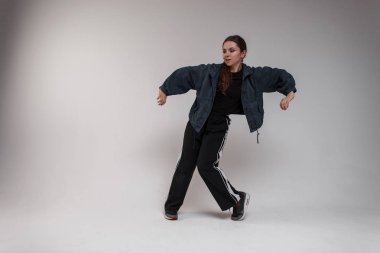 Şık genç güzel kadın dansçı bir gömlek moda siyah pantolon kot ceketli beyaz bir duvar yakınındaki Studio'da hip-hop dans ediyor. Modern koreografi. Yetenekli kız